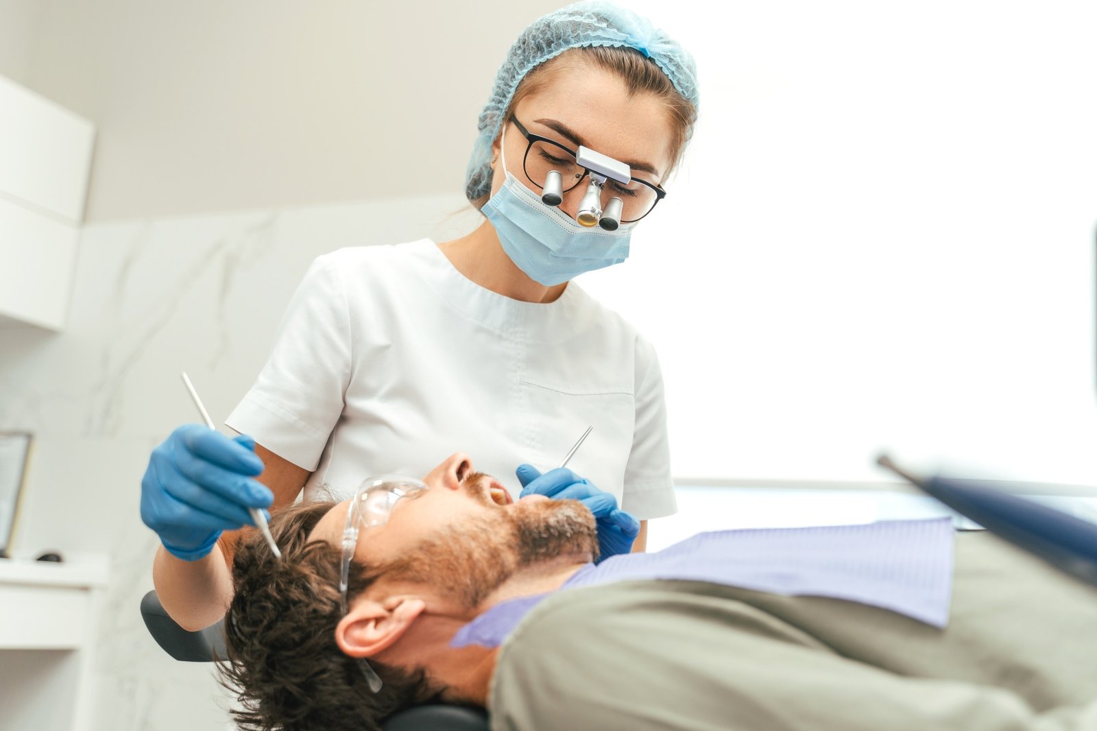Young bearded man having teeth check up by dentist during appointment